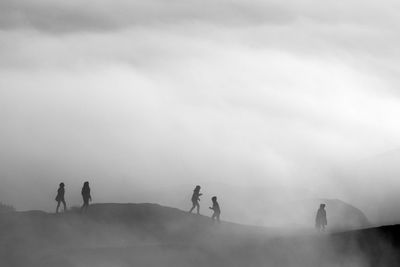 Silhouette of people walking on land amidst fog against sky