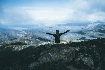 Woman sitting on rock against sky