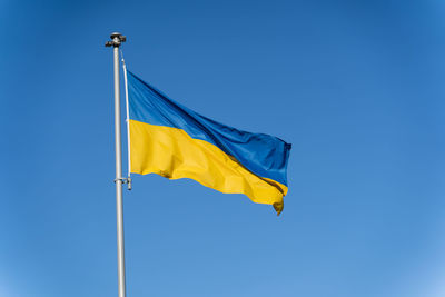 Blue-yellow ukrainian flag flies against the background of clear blue sky