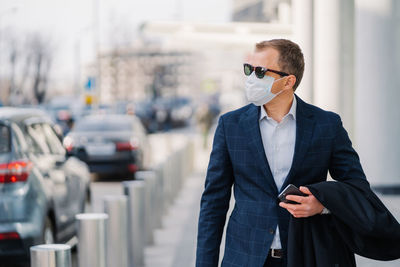 Businessman wearing mask walking on sidewalk in city