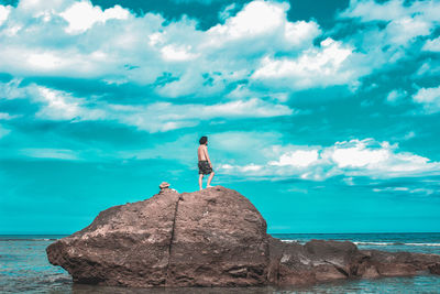 Shirtless man looking at sea while standing on rock against blue sky