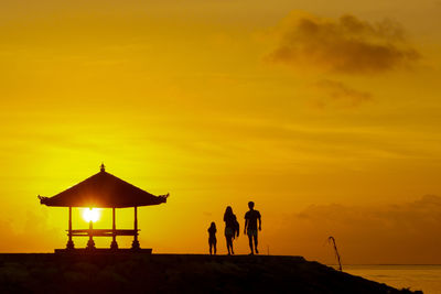 Silhouette family standing by gazebo at beach during sunset
