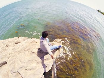 Rear view of man holding rock in sea