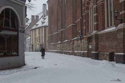 Man walking on snow covered street against buildings in city