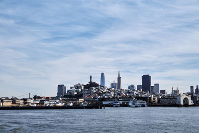 View of city at waterfront against cloudy sky