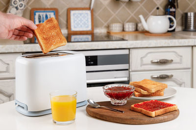 Male hand takes the toaster bread out of the white toaster. glass of orange juice