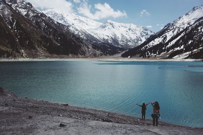 People on snowcapped mountains by lake against sky