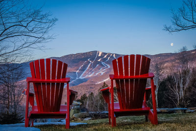 Red chairs on snow covered landscape against clear sky