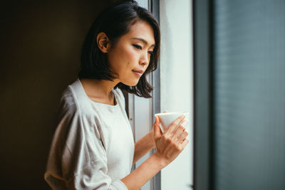 Young woman holding coffee while standing at home