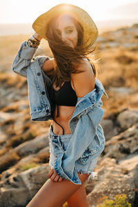 Thoughtful woman wearing hat while standing at beach during sunset