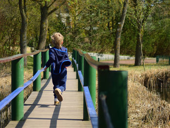 Rear view of boy running on footbridge at park