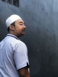 Side view of young man looking away against wall