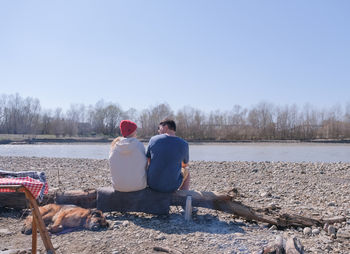 Rear view of couple sitting on beach against clear sky