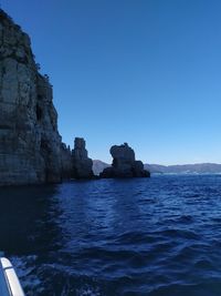 Rock formations in sea against clear blue sky