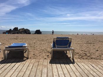 Empty lounge chairs at sandy beach against sky