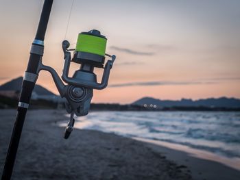 Close-up of fishing rod at beach against sky during sunset