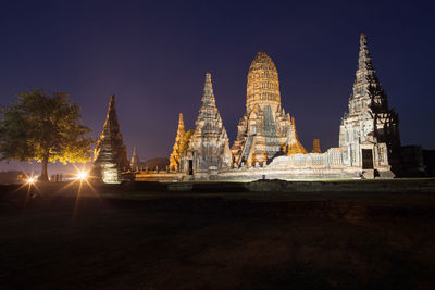 Illuminated temple by building against sky at night