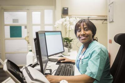 Portrait of mature female doctor with bangs working over computer while sitting in clinic