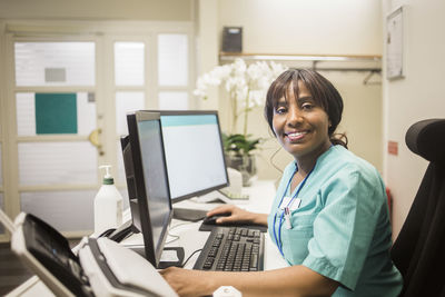 Portrait of mature female doctor with bangs working over computer while sitting in clinic