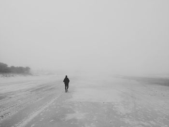 Rear view of man walking on snow covered land