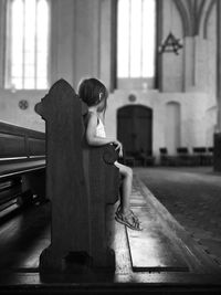 Side view of girl sitting on wooden bench in church