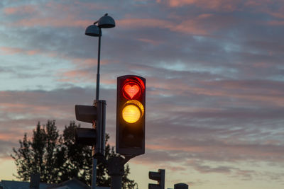 Low angle view of illuminated traffic signal against cloudy sky