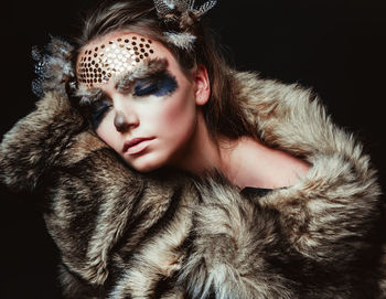 Close-up of young woman with make-up and fur against black background