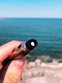 Close-up of hand holding pen against sea