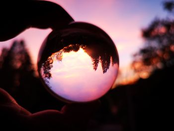 Close-up of hand holding crystal ball against sky during sunset