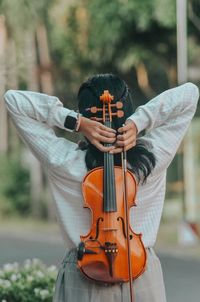 Rear view of woman holding violin outdoors