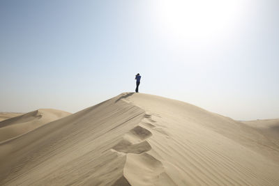 Low angle view of man walking on sand at desert against clear sky