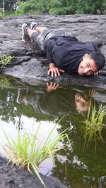 Portrait of young man lying on rock by pond