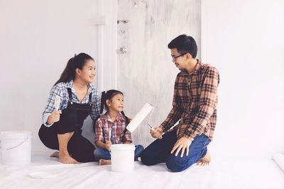 Full length happy family  sitting on floor painting color on wall house.