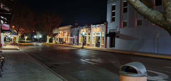 Illuminated street amidst buildings in city at night