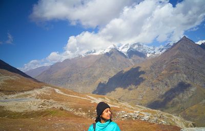 Mid adult woman sitting on mountain against cloudy sky during sunny day