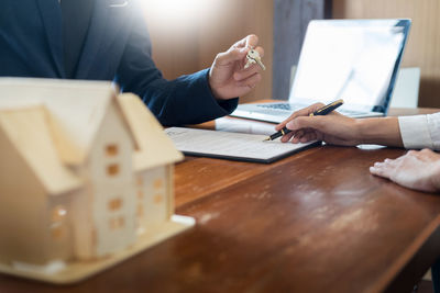 Midsection of agent giving key to woman at desk in office