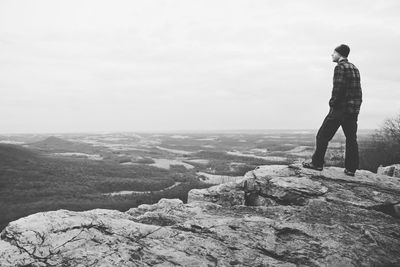 Man standing on rock by sea against sky