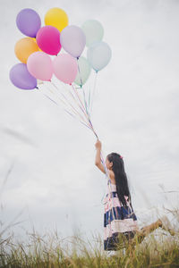 Low angle view of woman holding balloons on field against sky