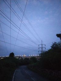 Electricity pylon by road against sky at dusk