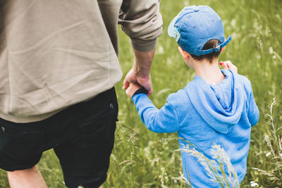 Rear view of father holding son hands while walking on land