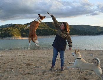 Young woman playing with dogs at lakeshore during sunset