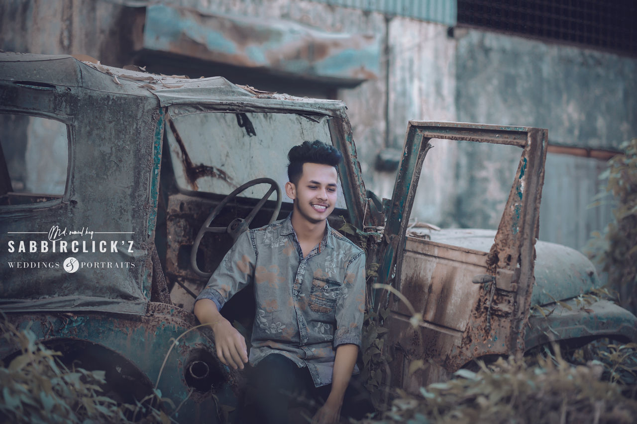 PORTRAIT OF A SMILING YOUNG WOMAN SITTING IN ABANDONED CAR