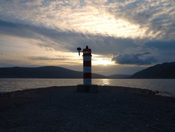 Lighthouse by sea against sky during sunset