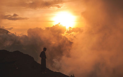 Rear view of silhouette man photographing against sky during sunset