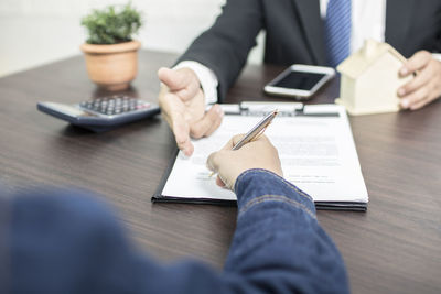 Midsection of man pointing at paper for customer to sign on desk