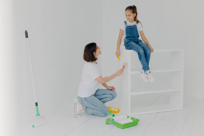 Full length of mother and daughter holding paint roller sitting at home