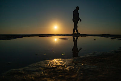 Silhouette man standing by sea against sky during sunset