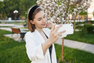 Young woman taking selfie with smart phone while standing in park