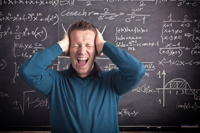 Frustrated teacher screaming against blackboard in classroom