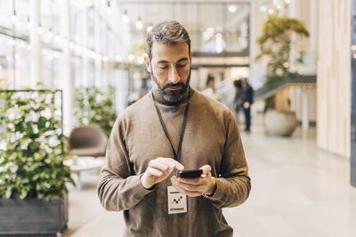 Mature businessman using phone while standing at convention center